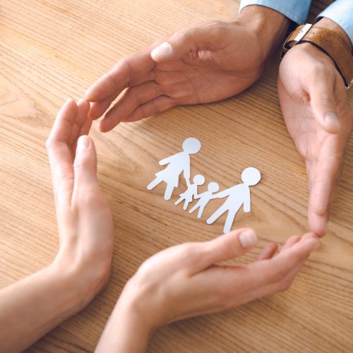partial view of insurance agents and female hands with family paper model on wooden tabletop, family